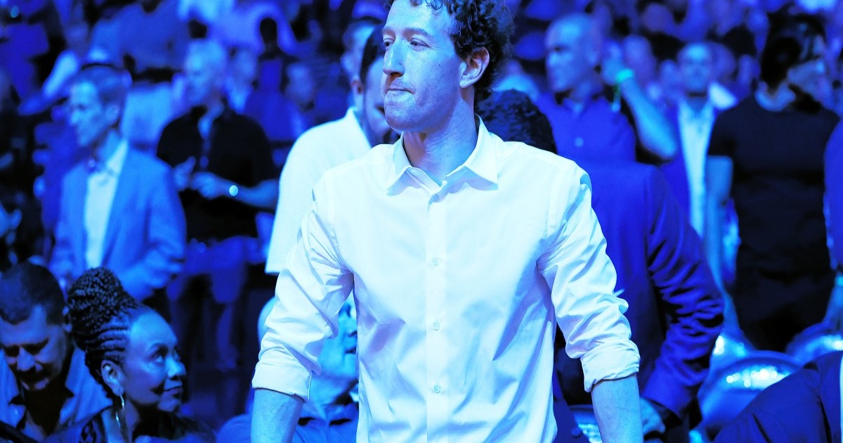 Mark Zuckerberg dengan ekspresi serius di tengah kerumunan, latar biru
